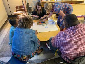 Montessori instructors sit around a table while going over guided sessions on how to use Montessori resources effectively.