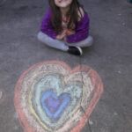 student sitting by rainbow chalk art